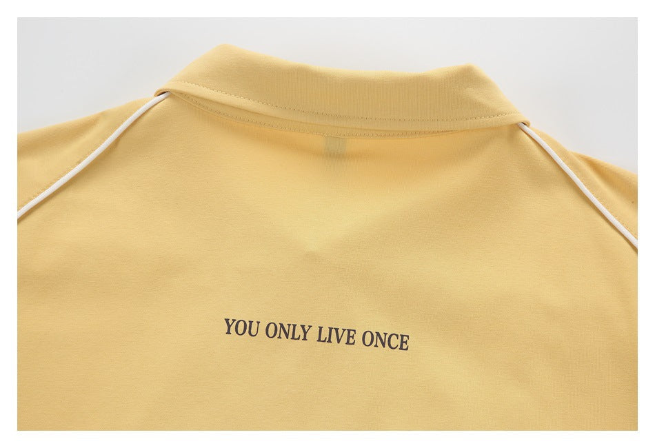 Close-up of a pale yellow collared top with white shoulder piping and the printed text “YOU ONLY LIVE ONCE.”