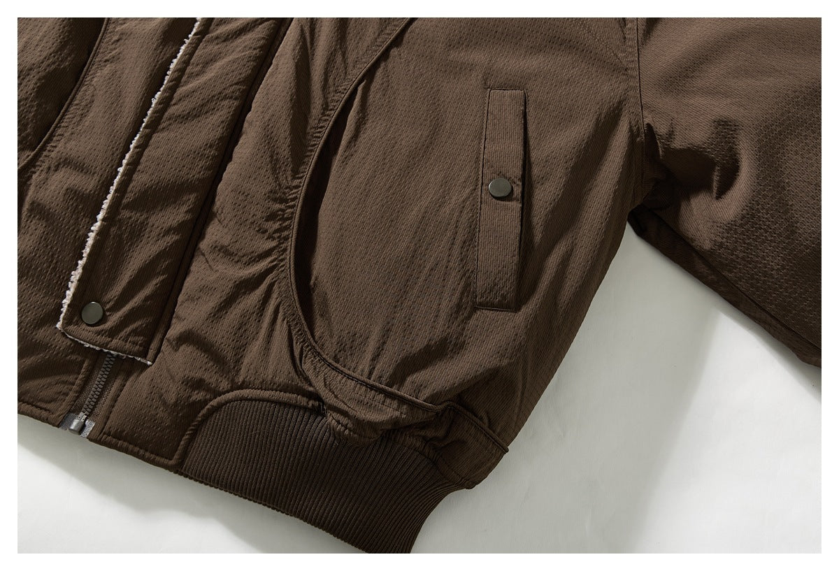 Close-up of a brown jacket sleeve and snap-tab pocket, with the ribbed hem and zipper edge visible.
