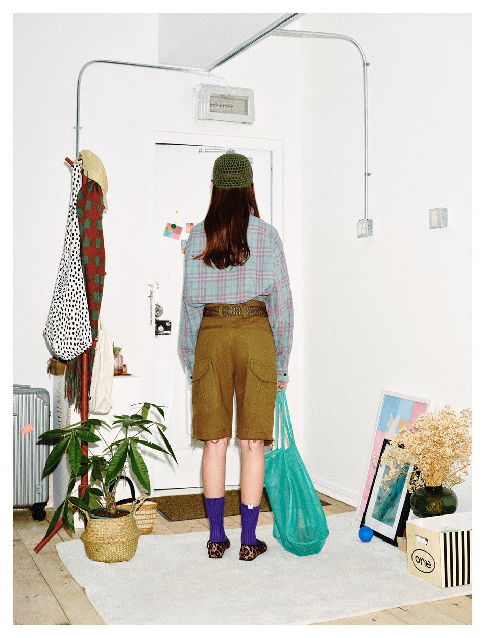 Rear view of a model wearing a pastel plaid shirt, olive cargo shorts, purple socks and a green knit cap.