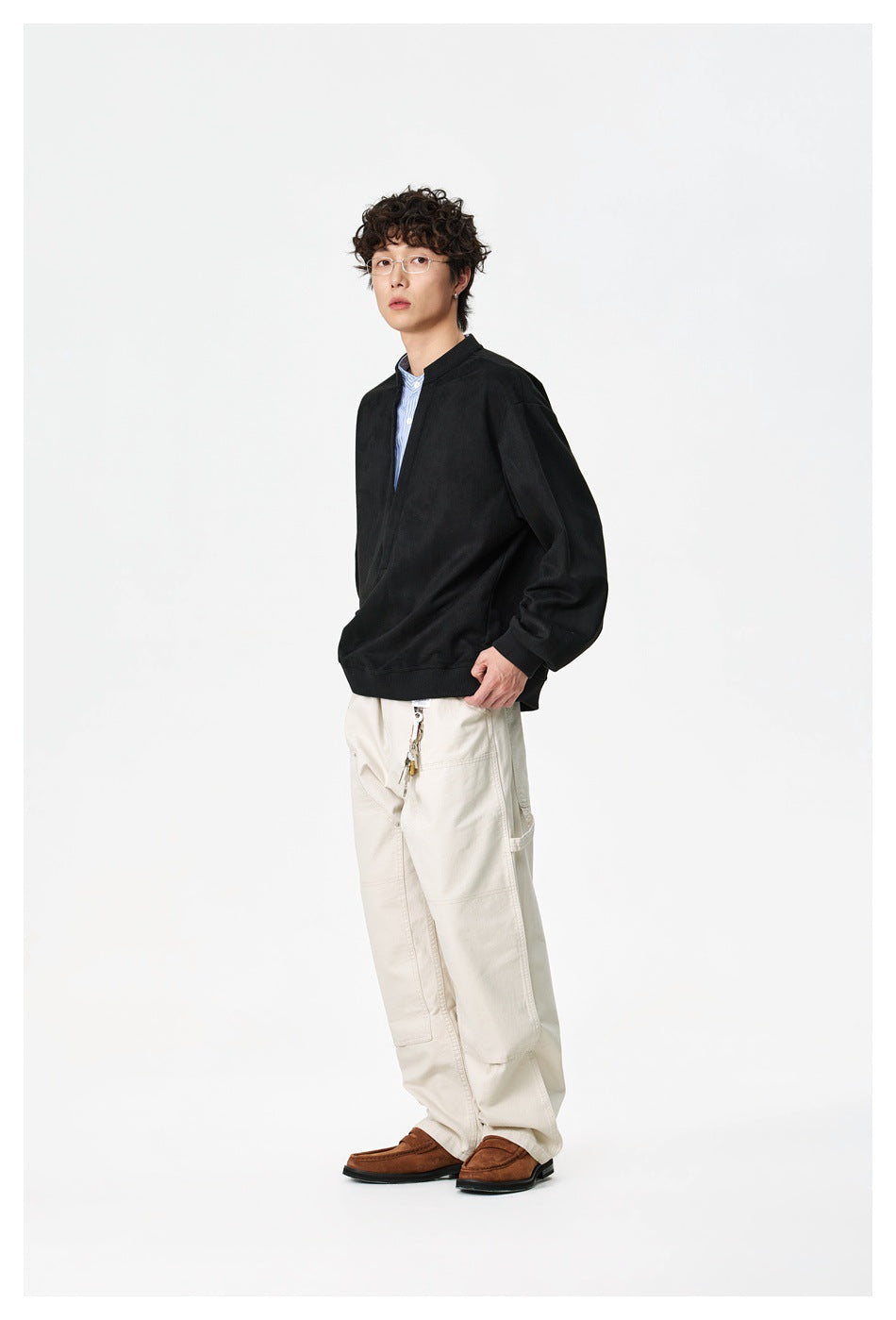 Full-length three-quarter view of a model wearing a black oversized split-neck pullover and cream trousers.