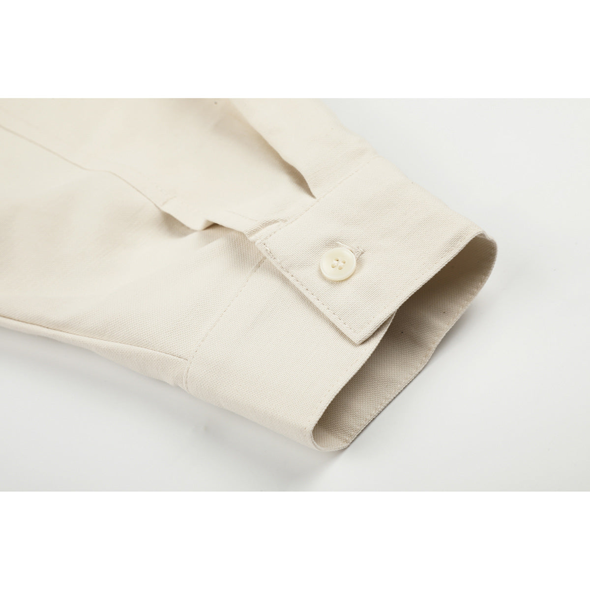 Close-up of an ivory shirt cuff with a button and visible seam stitching.