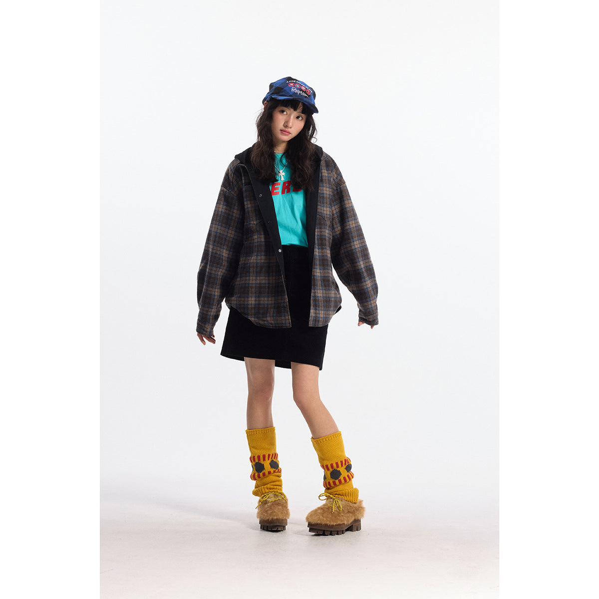 Front view of a model in an oversized brown-and-blue plaid shirt jacket over a black skirt and turquoise top.
