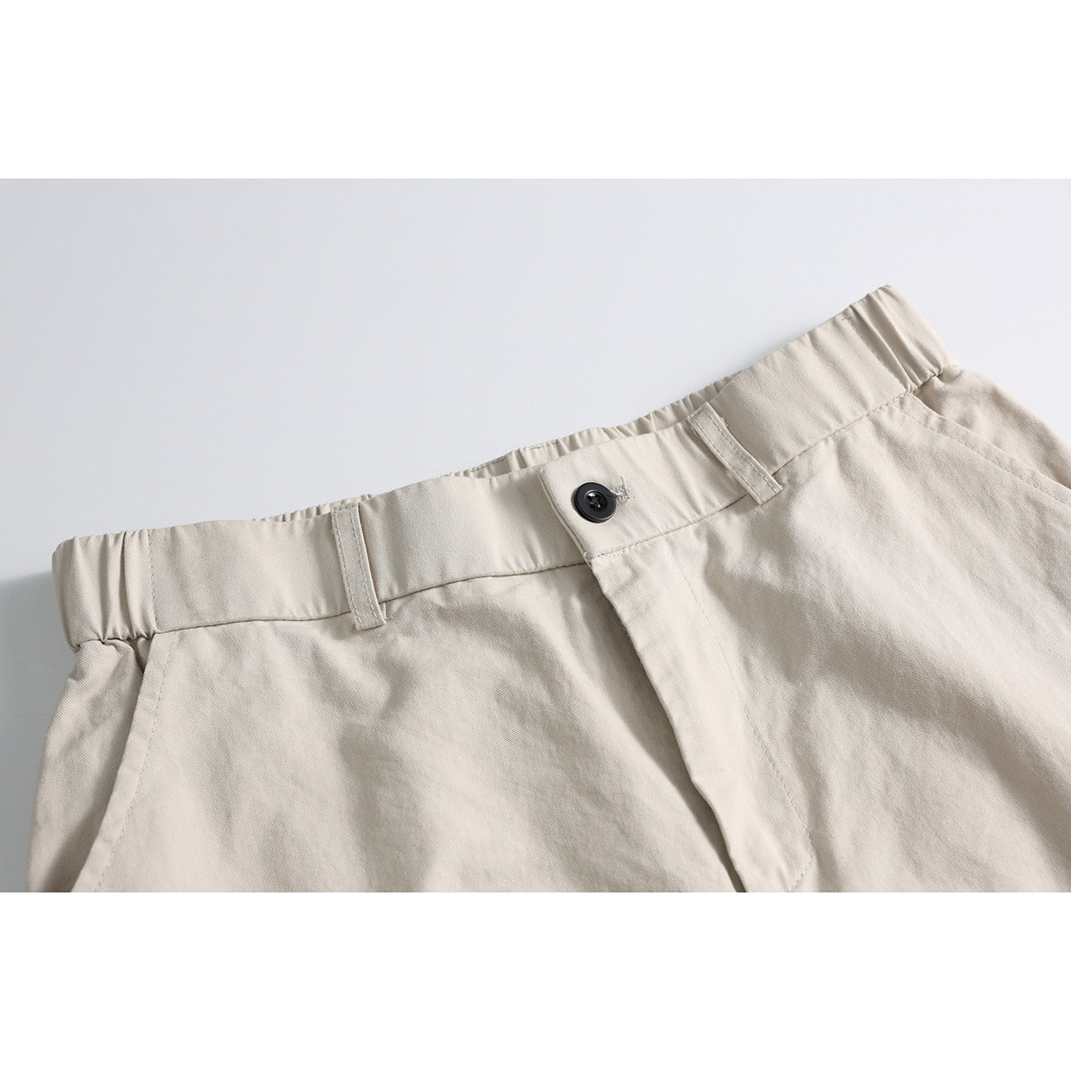 Close-up of light beige cargo shorts showing the gathered waistband, belt loops, black button and fly.