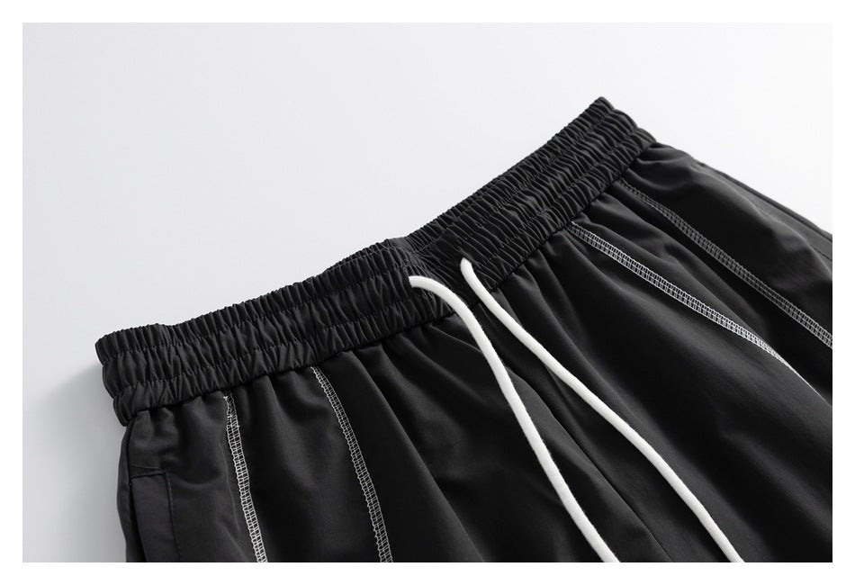 Close-up of black shorts showing the gathered waistband, white drawstrings, and contrast stitching.