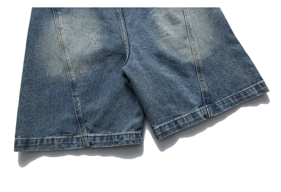 Blue denim shorts laid flat, showing the front crotch seam, faded wash, and wide leg hems.