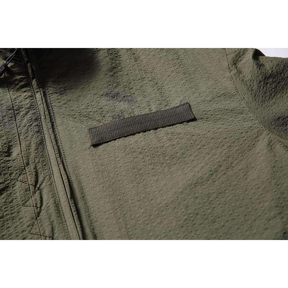 Close-up of textured olive-gray jacket fabric and a narrow dark chest tab near the zipper.