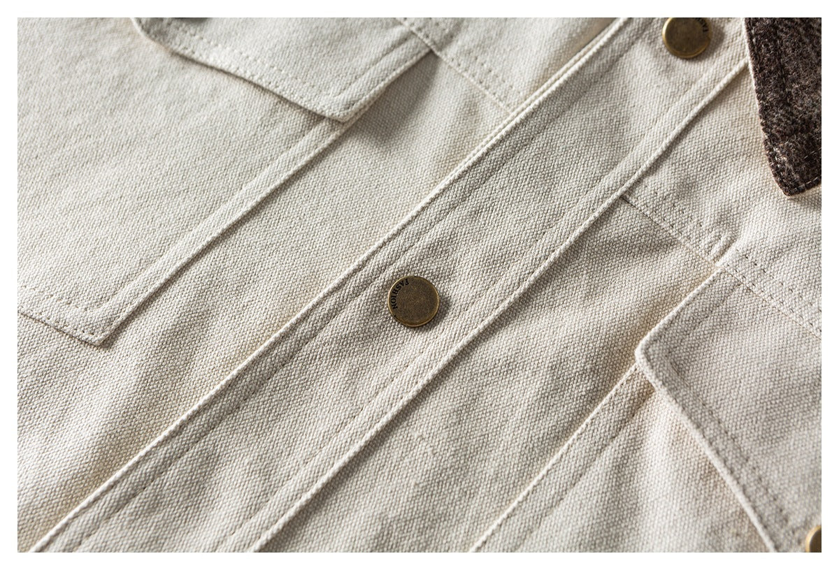 Close-up of a beige shirt front placket with a brass button, stitched pockets and a glimpse of plaid trim.