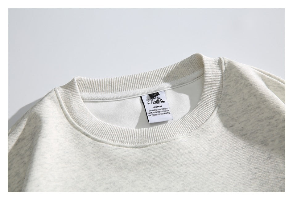 Close-up of the ribbed crew neckline and inner label on an off-white heathered sweatshirt.