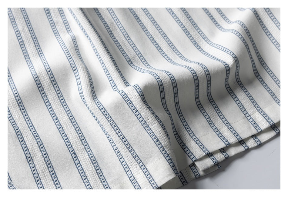 Close-up of draped white shirt fabric with repeating narrow blue stripes and a stitched edge.
