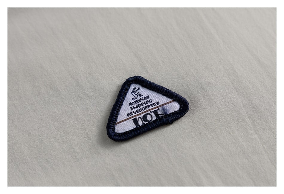 Close-up of a triangular embroidered patch with dark edging on beige jacket fabric.