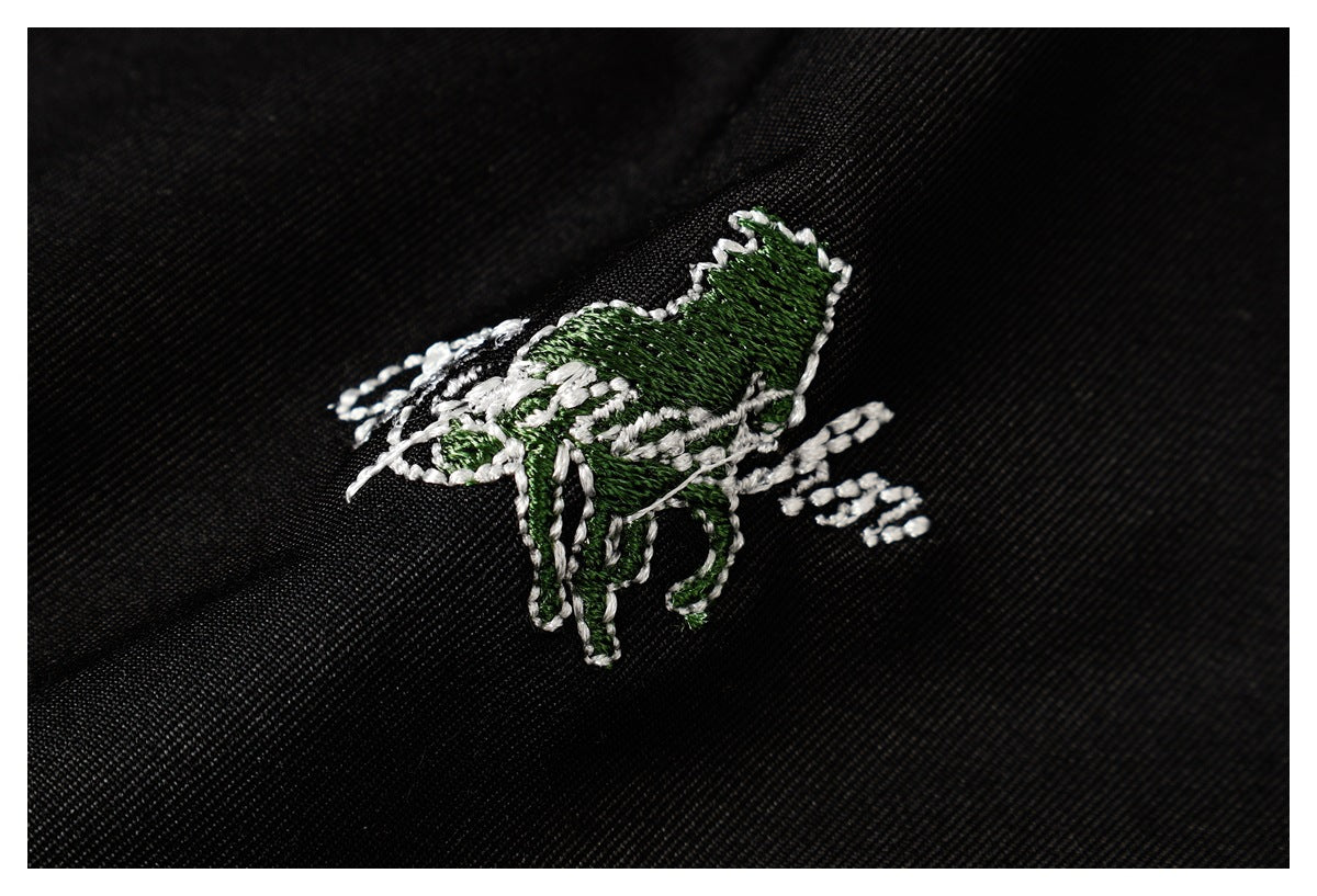 Close-up of a green-and-white embroidered animal emblem on black fabric.