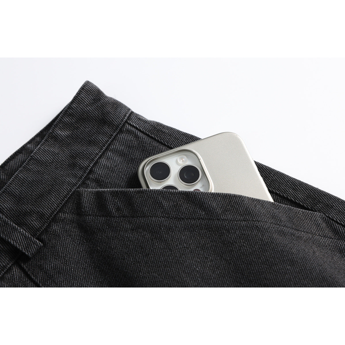 Close-up of a deep pocket in charcoal-black denim trousers holding a silver smartphone.