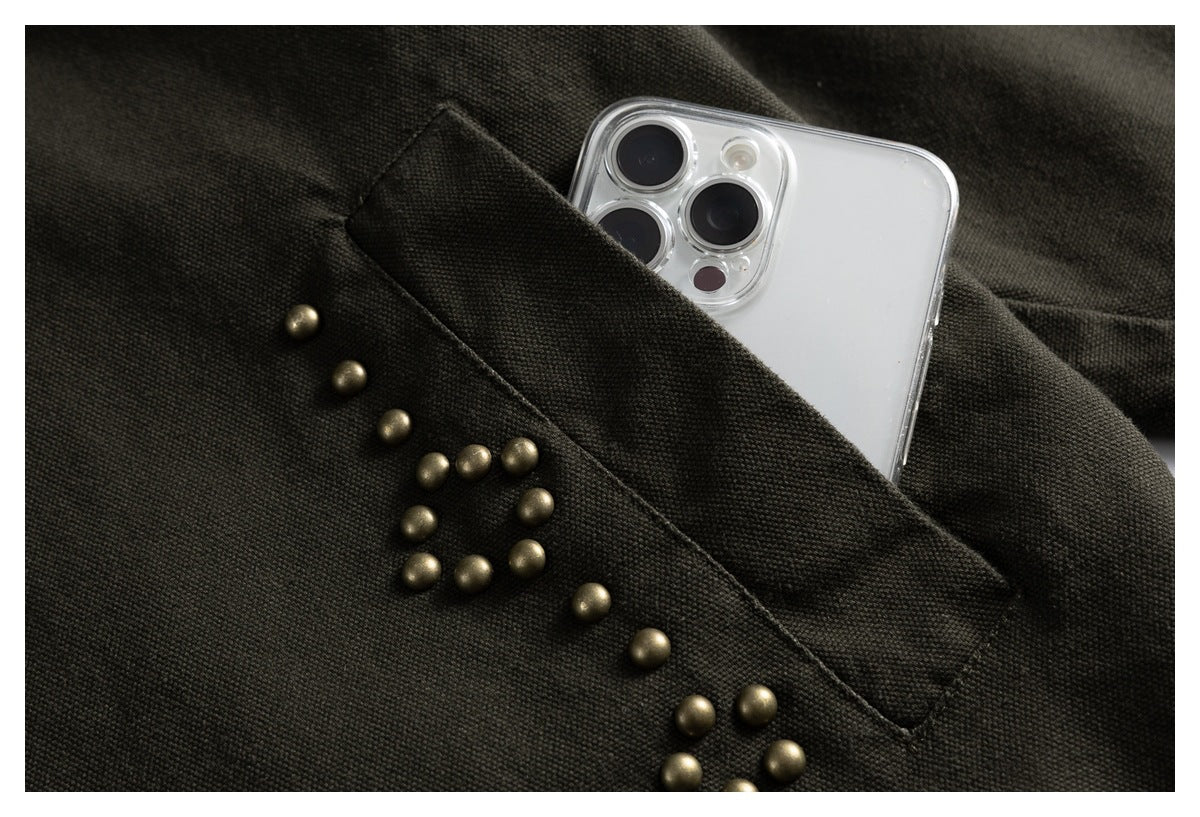 Dark olive jacket pocket with brass stud embellishments; a phone is tucked inside.