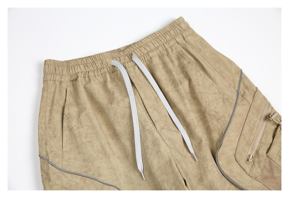 Close-up of the tan pants' elastic waistband, white drawstrings, gray piping, and zippered side pocket.