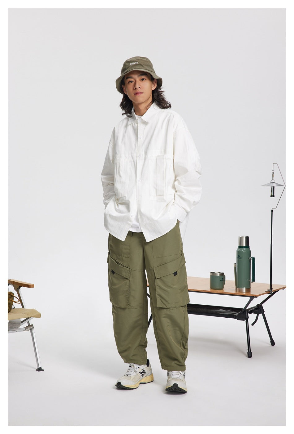 Full-length model wearing a loose white button-up shirt with two large front pockets and olive cargo pants.