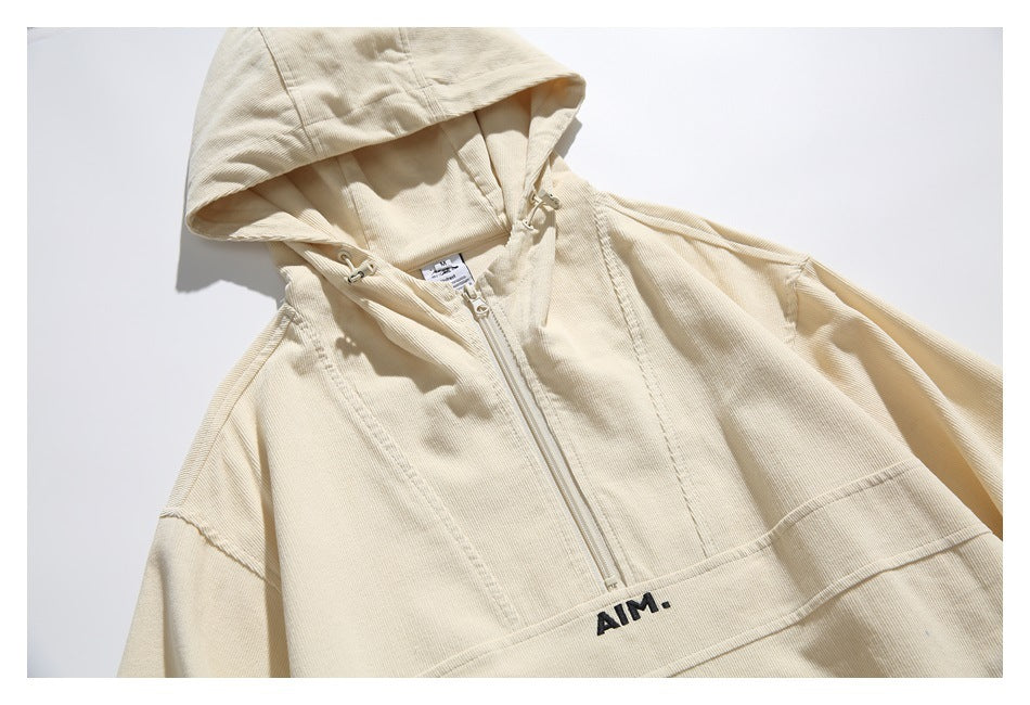 Close-up of a cream hooded pullover with a front zipper, drawcord hood, and black AIM lettering.