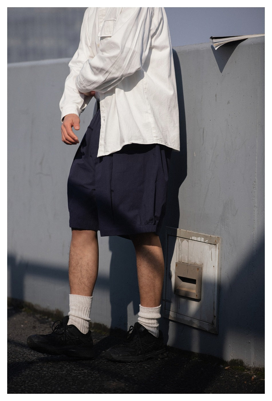 Close view of a model wearing loose navy shorts with an elastic waist and a white shirt.