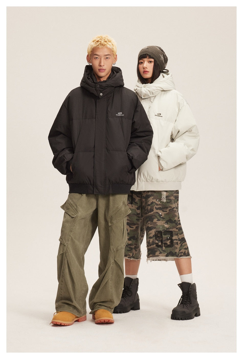 Two models wearing hooded puffer jackets in black and off-white with hoods up and hands in pockets