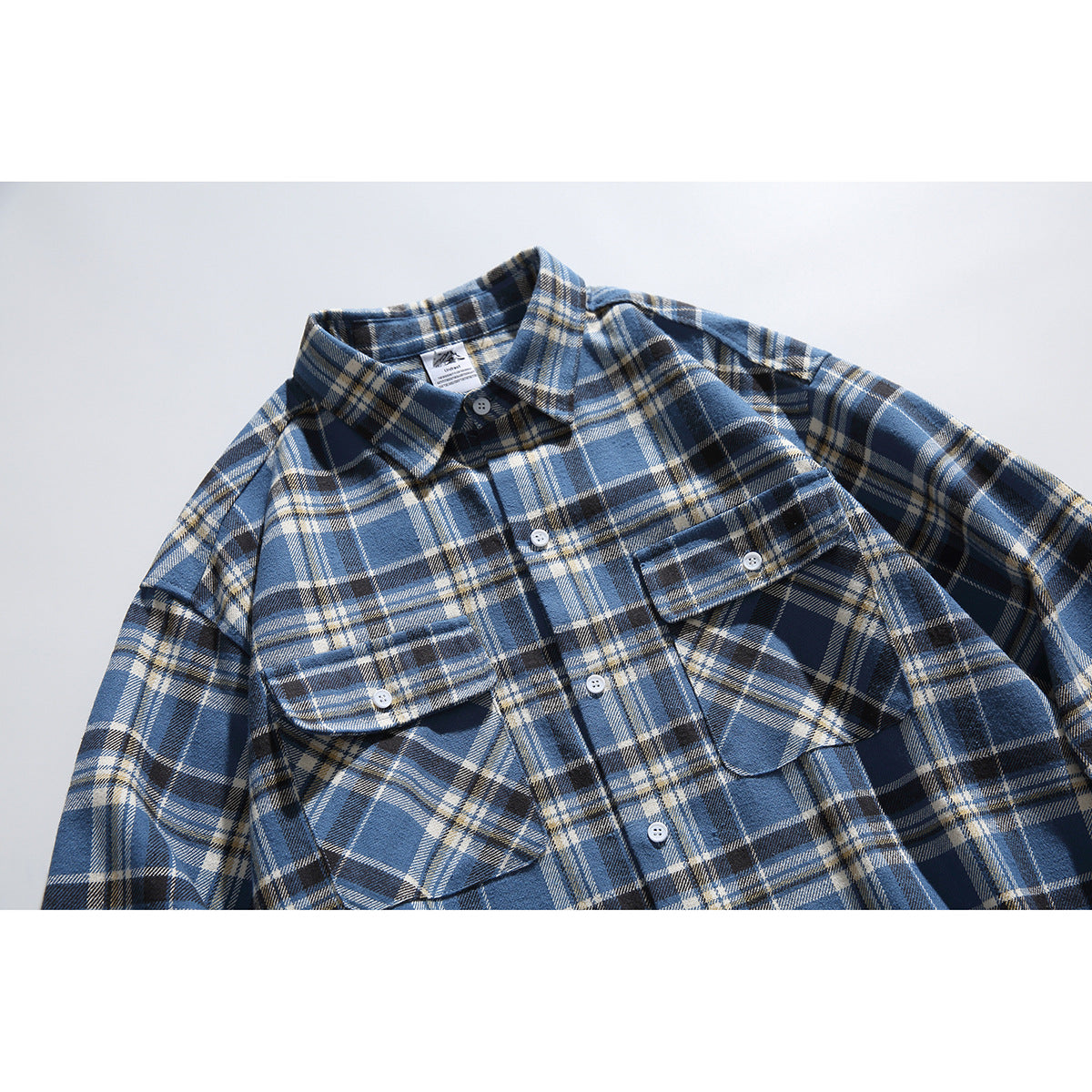Front view of a blue, navy, and cream plaid button-up shirt with two flap chest pockets and white buttons.