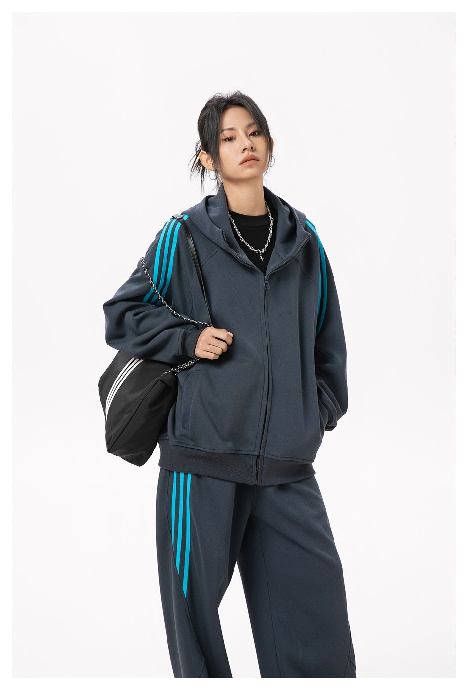 Model wearing a charcoal hooded zip jacket and matching pants with bright cyan side stripes; upper-body view.