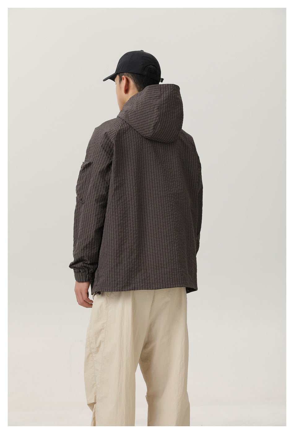 Back view of model wearing dark checked hooded jacket with beige pants, showing hood and check pattern