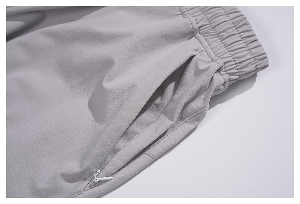 Close-up of light gray trousers showing a slanted zip pocket and gathered elastic cuff.