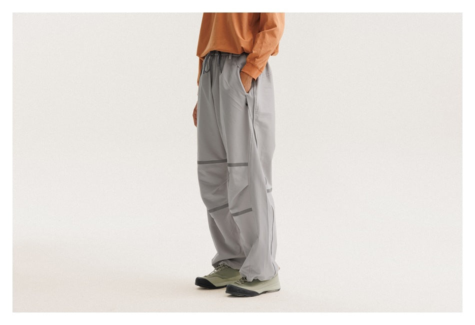 Cropped side view of a model wearing loose light-gray drawstring pants with dark bands across the legs.
