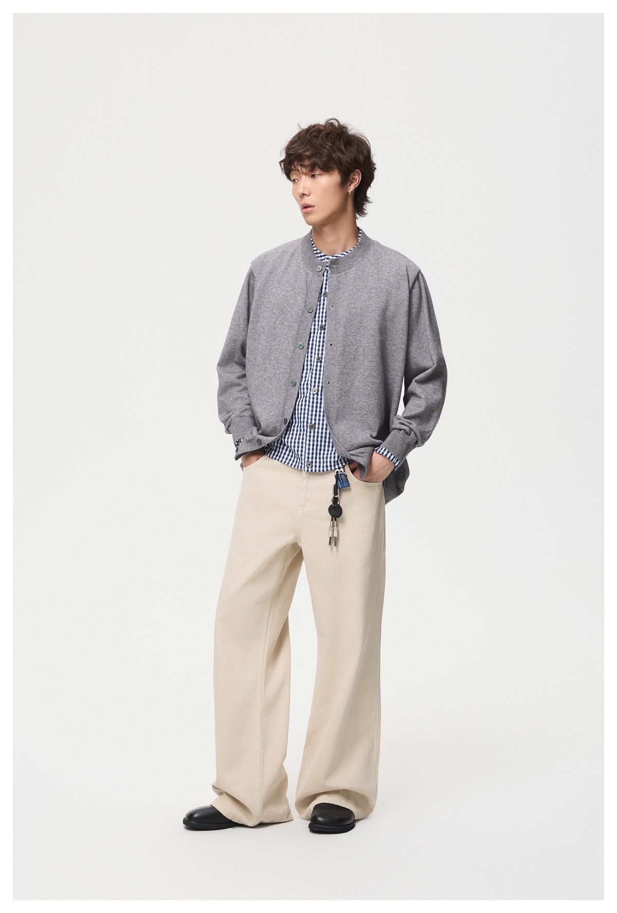 Full-length model wearing a gray cardigan over a blue-and-white checked shirt with wide cream trousers.