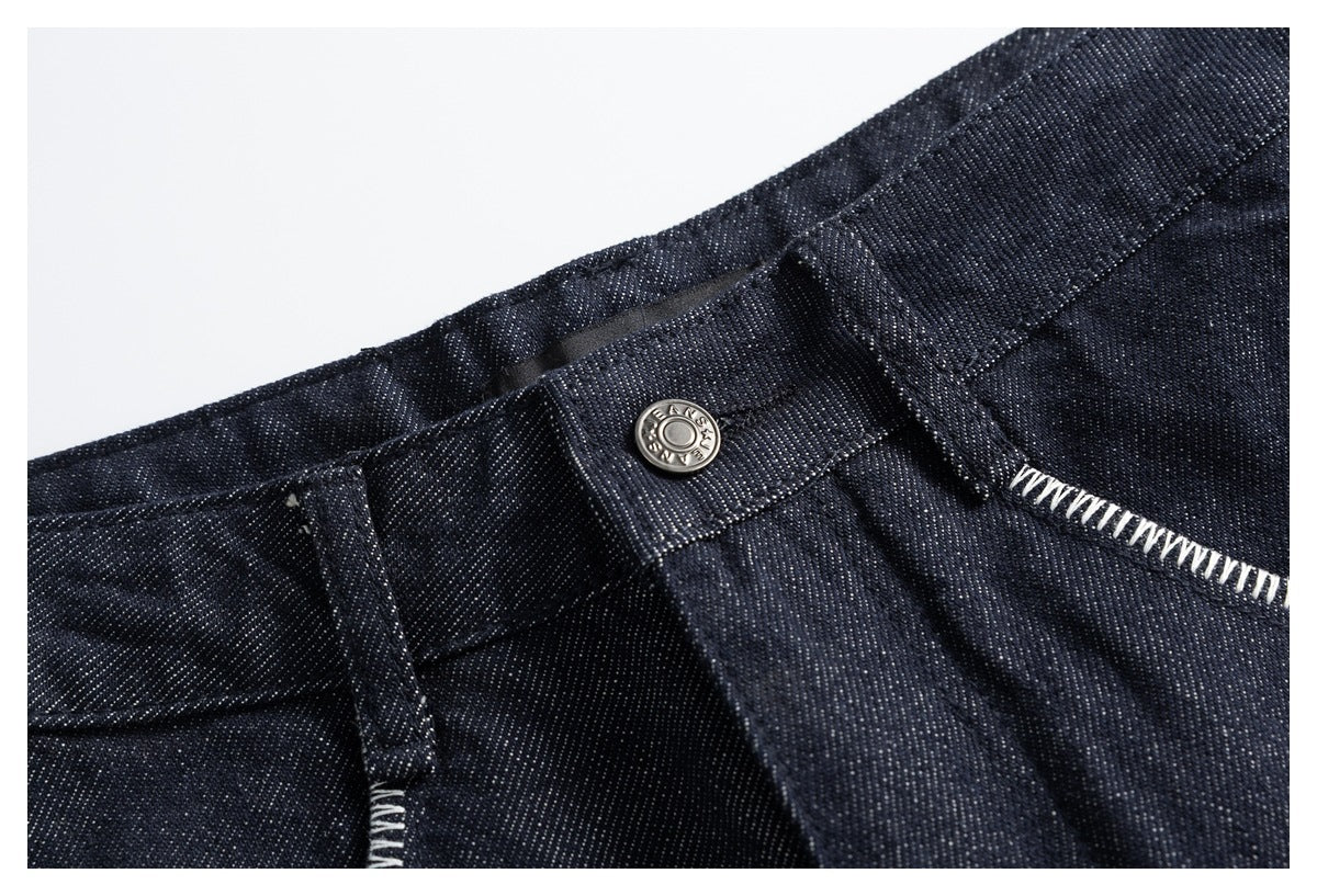 Close-up of dark indigo denim trouser waist with a metal button, belt loop, fly and contrasting white pocket stitching.
