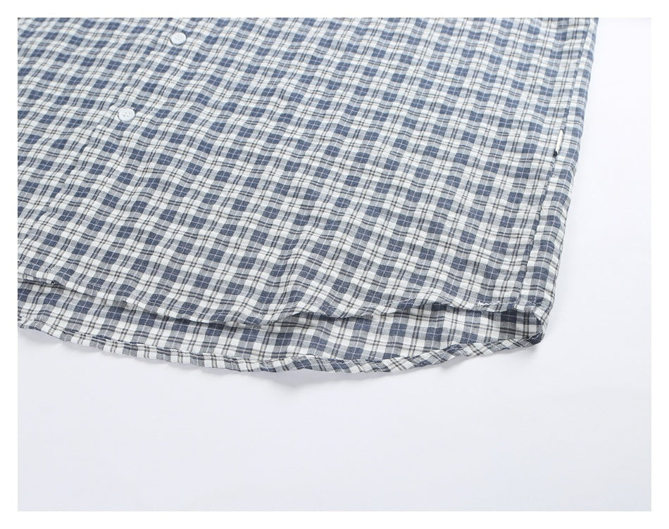 Close-up of the curved hem and buttons on a blue, gray, and white plaid shirt.