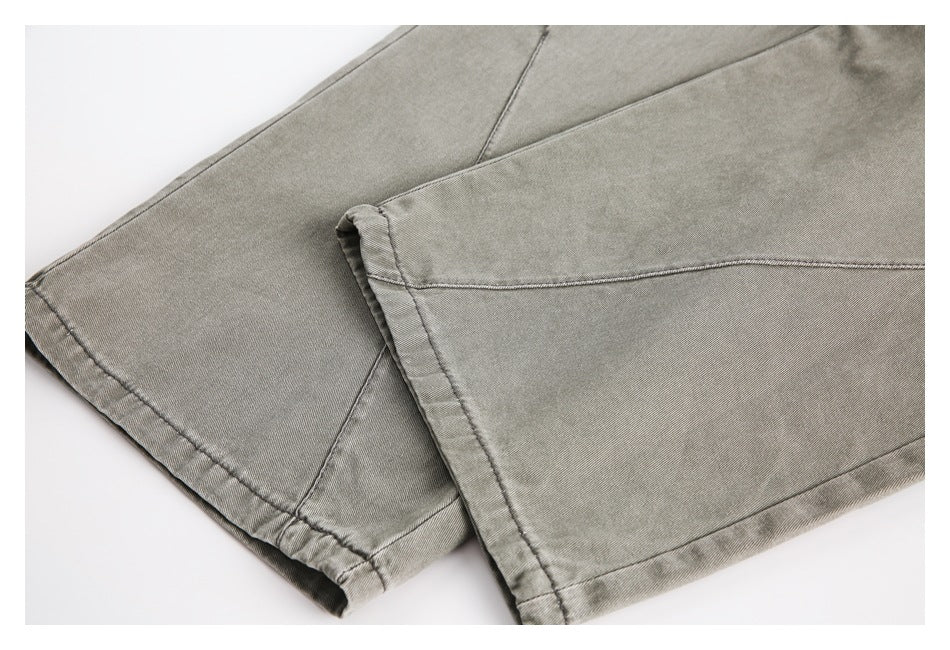 Close-up of the stitched hems and leg seams of gray-olive trousers.