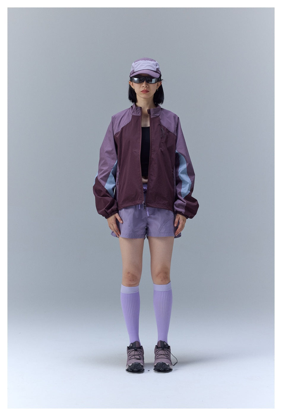 Woman wearing a burgundy and lavender color-block jacket with pale sleeve stripes, shown from the front.