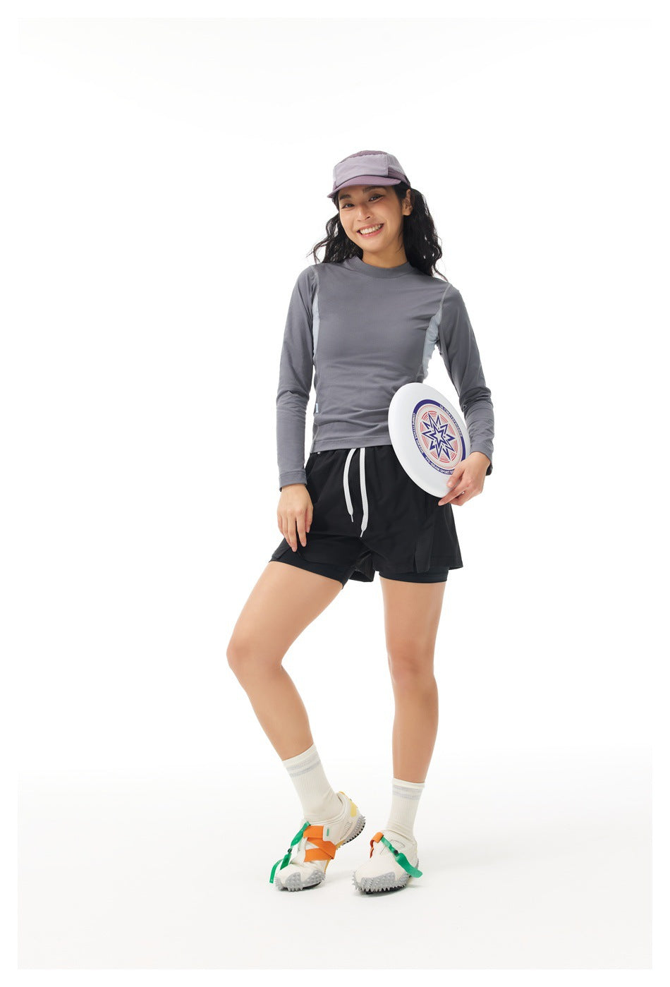 Model wearing a gray long-sleeve top and black shorts, holding a white flying disc.