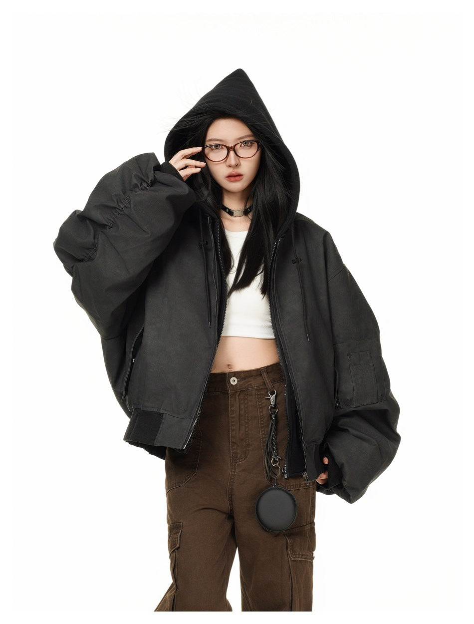 Front view of a model wearing a black oversized hooded jacket with a zip front, voluminous ruched sleeves and flap pockets.