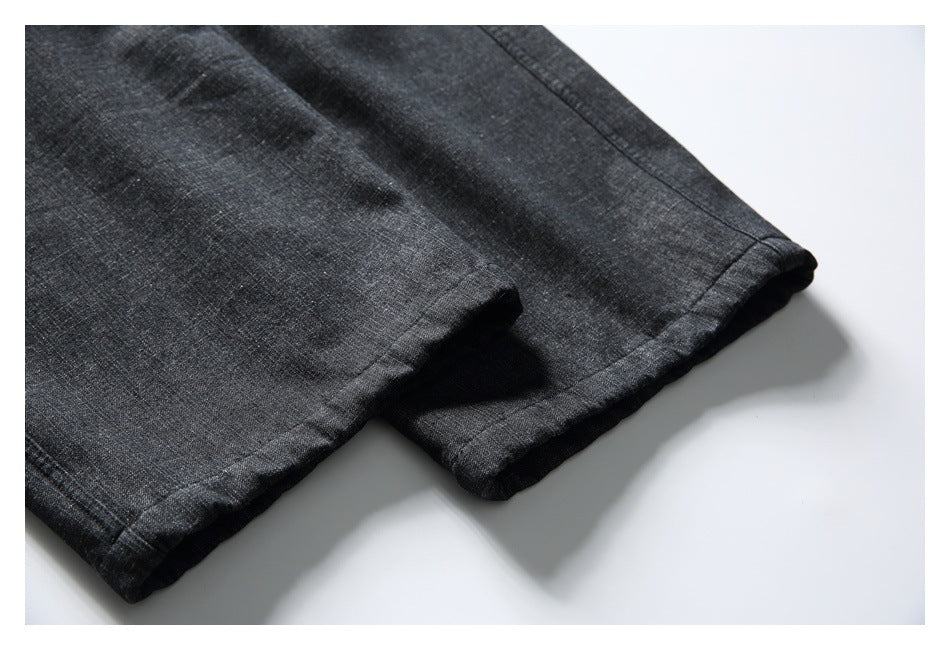 Close-up of the stitched hem on black textured trouser legs against a white background.