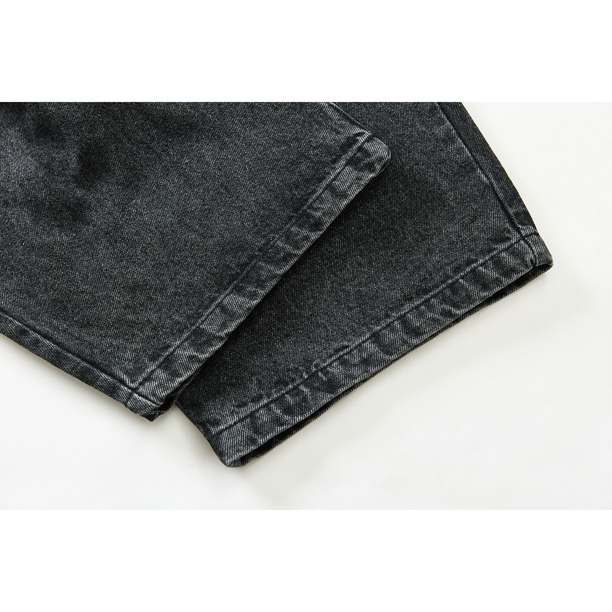Close-up of the legs and double-stitched hems of black washed denim trousers.
