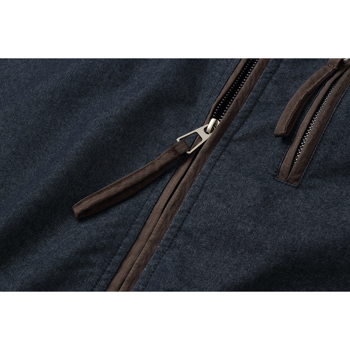 Close-up of the dark indigo jacket's front zipper and brown-trimmed zip pocket with metal pulls.