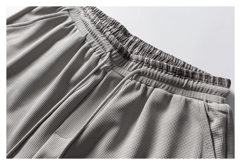 Close-up of light gray textured trousers showing the elastic waistband and gathered fabric.