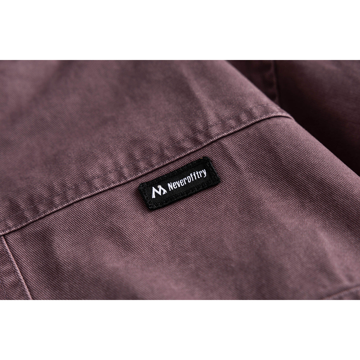 Close-up of a black brand patch stitched onto plum jacket fabric.