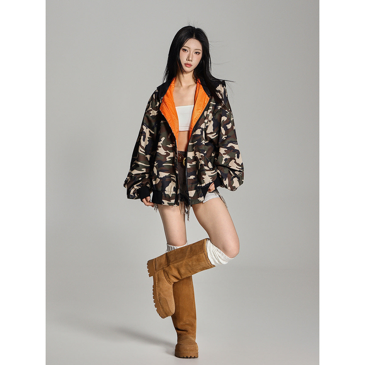 Full-length model wearing an open camouflage jacket with orange lining, black trim and oversized sleeves.