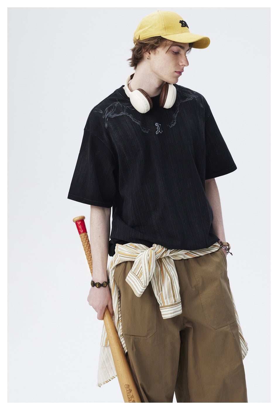 Model wearing a black oversized graphic T-shirt with a small chest emblem, shown from the front.