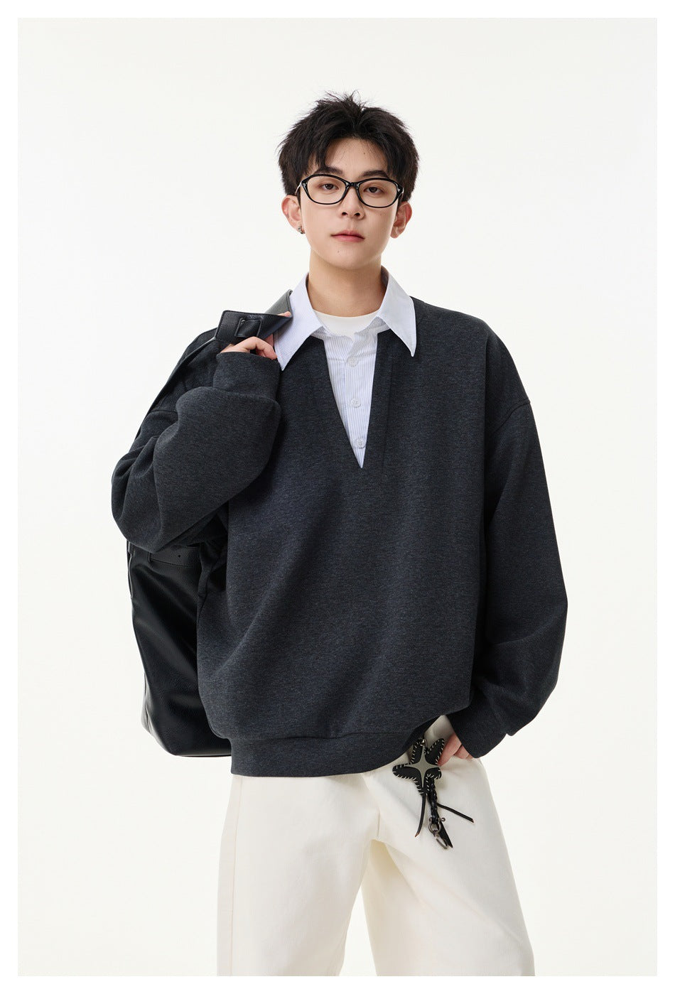 Model wearing an oversized charcoal V-neck pullover over a white collared shirt, with white trousers.
