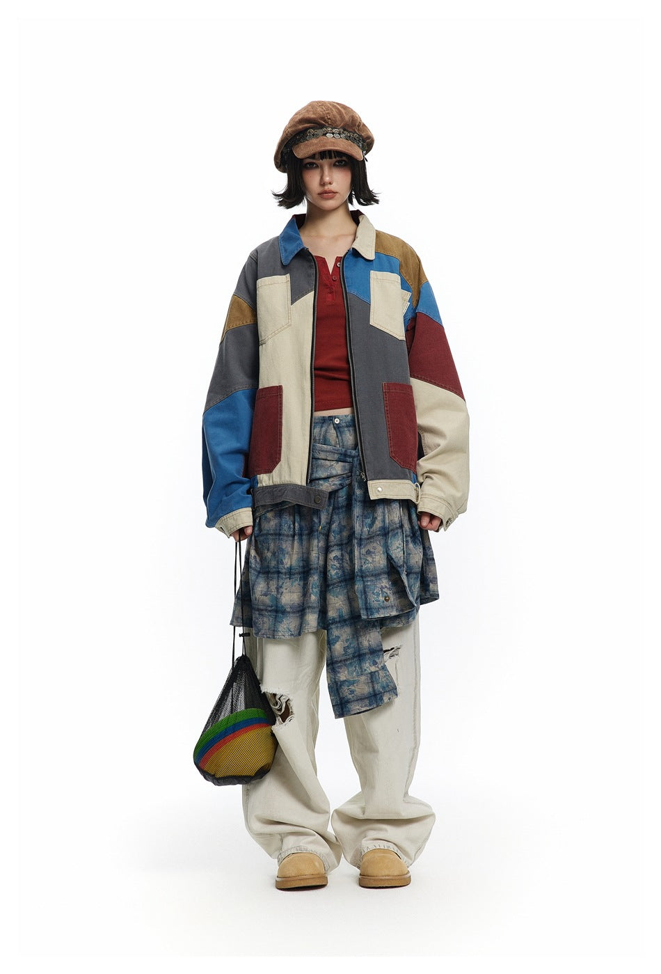 Front view of a model wearing a multicolor patchwork jacket with a blue patterned skirt and loose cream trousers.