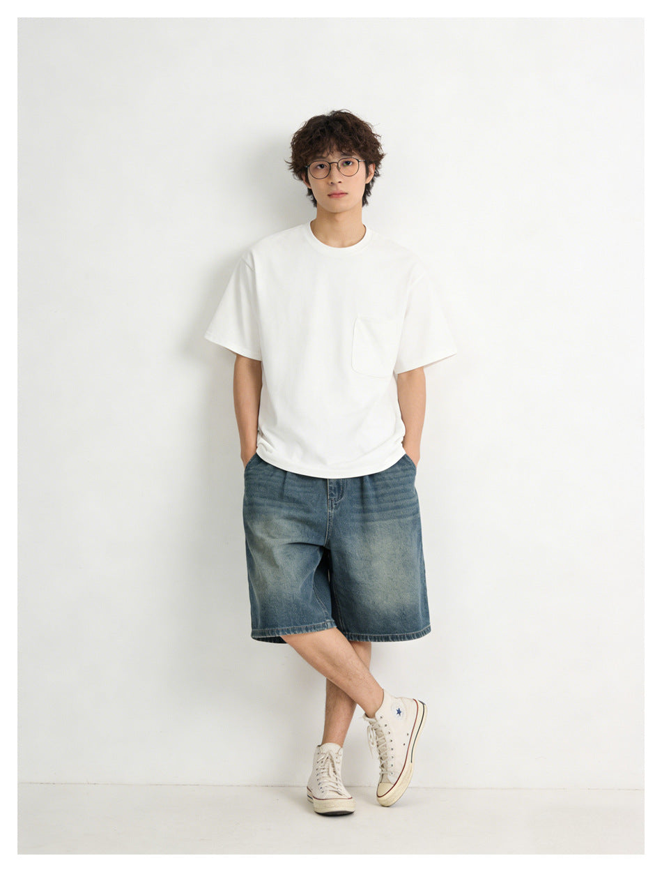 Model wearing a white pocket T-shirt with loose blue denim shorts and white high-top sneakers.