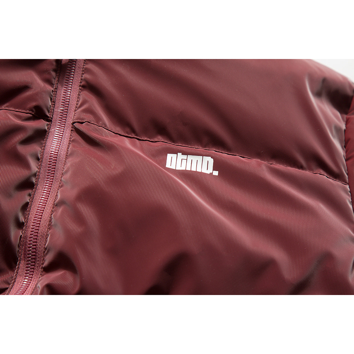 Close-up of a burgundy puffer jacket with a small white chest logo and front zipper.