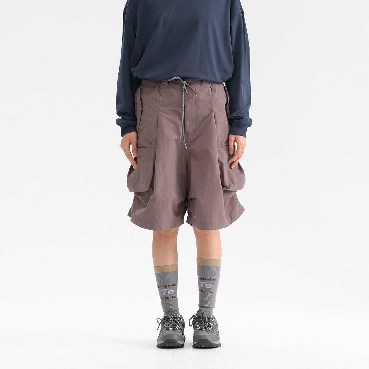 Front view of a model wearing mauve-gray wide cargo shorts with a drawstring waist and oversized side pockets.