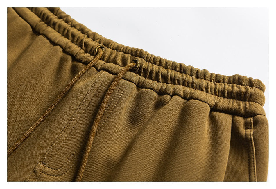 Close-up of ochre joggers showing an elastic waistband, drawcords, and front pocket stitching.