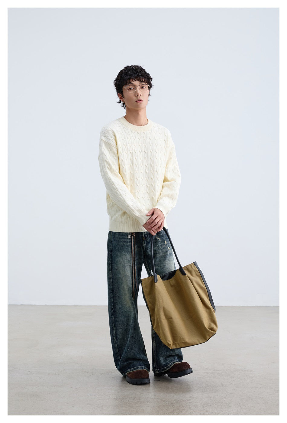 Model wearing an ivory cable-knit crewneck sweater with ribbed cuffs and hem.