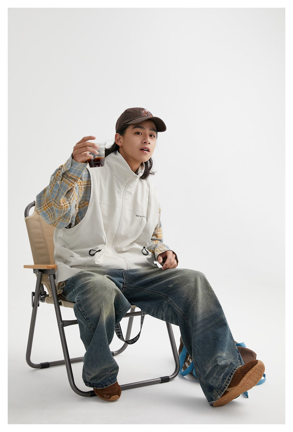 Seated model wearing an off-white high-collar zip vest over a blue and ochre plaid shirt.