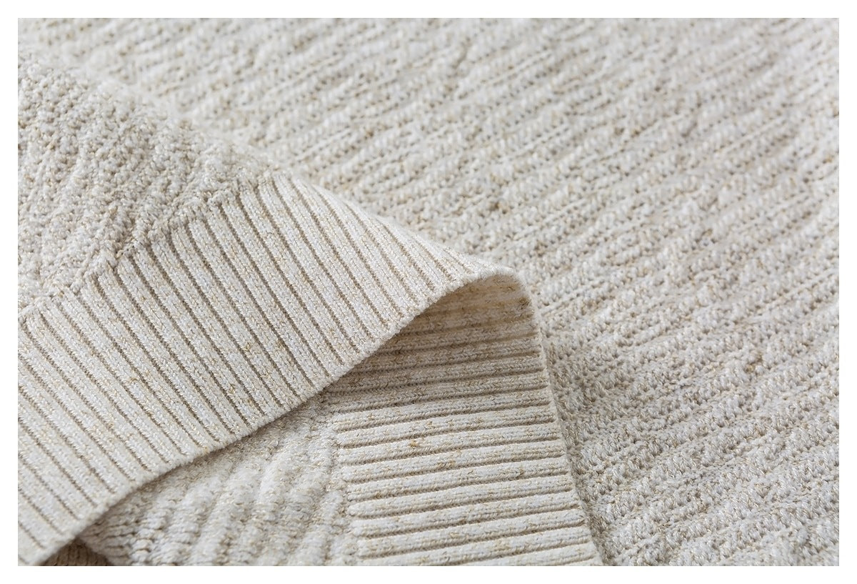 Close-up of a folded ribbed edge against the cream textured knit fabric.